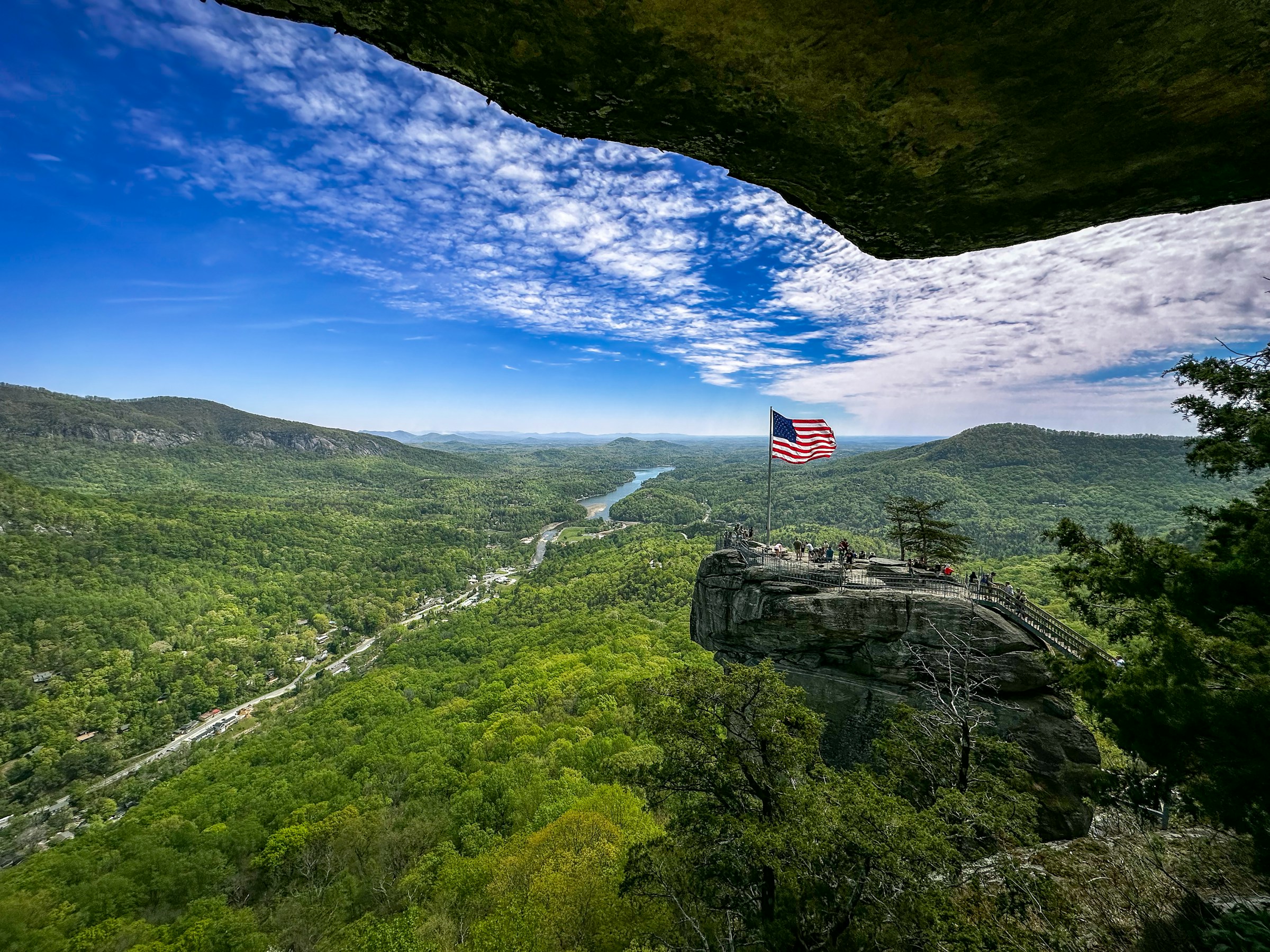 American flag waves above cliff and beautiful green scenery