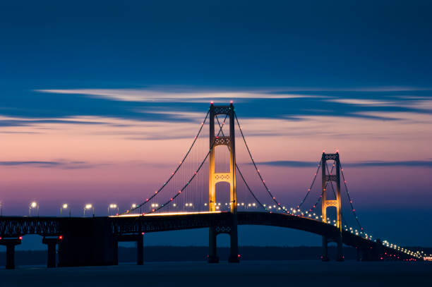 The Mackinac Bridge illuminated with lights against a purple night sky
